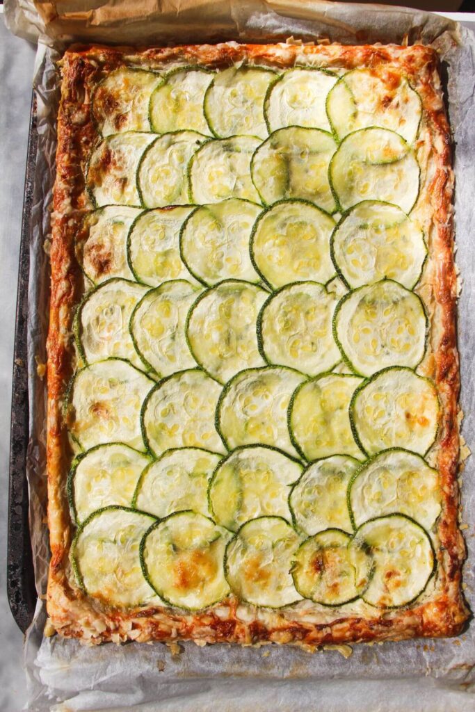 Zucchini puff pastry tart baked on a lined oven tray.