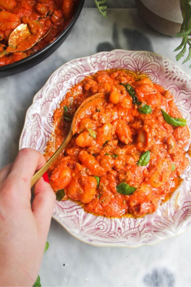 Creamy tomato sausage gnocchi on a pink plate with a gold spoon.