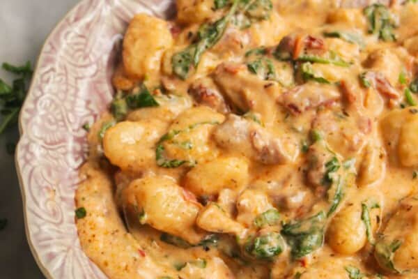Close up of creamy chicken gnocchi on a small pink plate with another plate in the background.