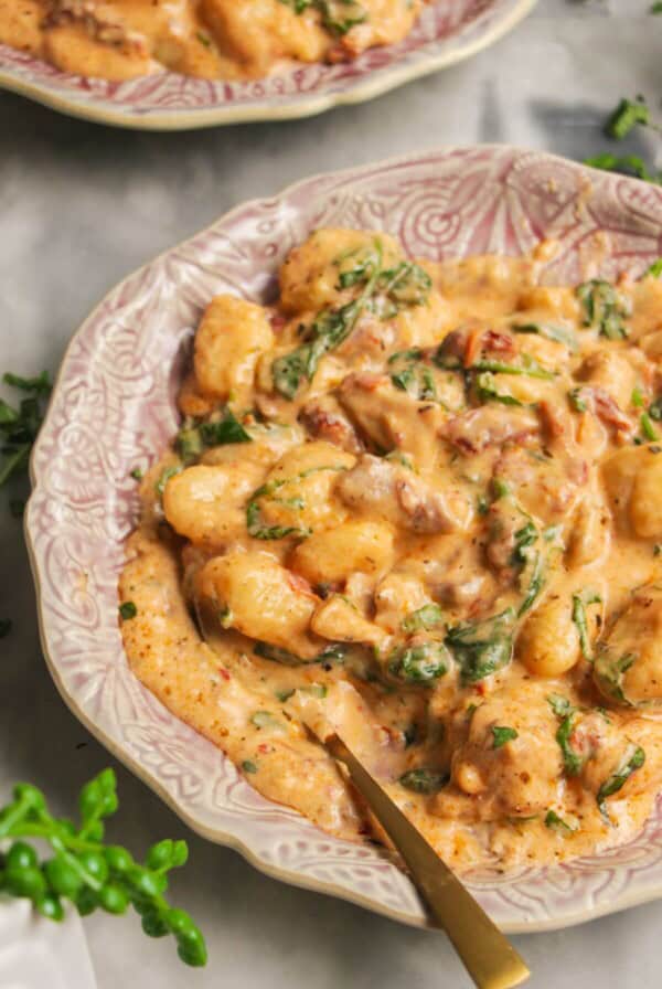 Close up of creamy chicken gnocchi on a small pink plate with another plate in the background.
