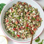 Greek quinoa salad in a large white salad bowl with feta on the side.