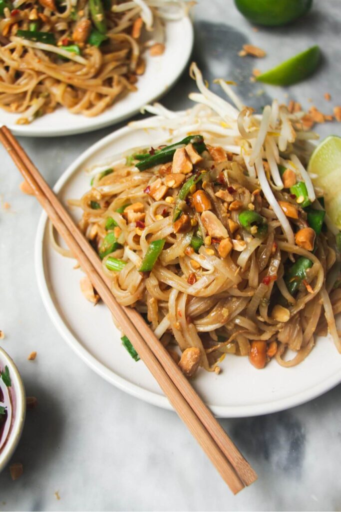 Close up of a pile of Pad Thai on a small white plate with chopsticks on the side.