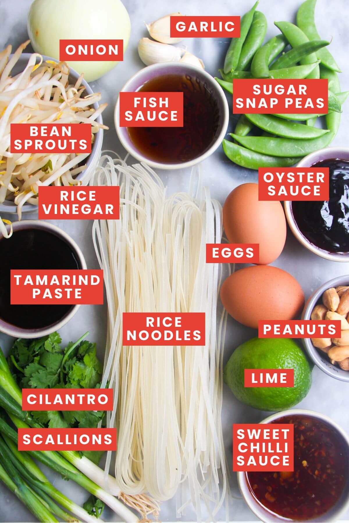 Ingredients for Pad Thai laid out on a marble background and labelled.