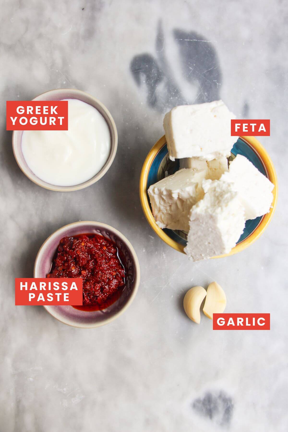 Ingredients for spicy feta dip laid out on a marble background and labelled.