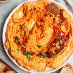 Spicy harissa feta dip on a small white plate, with bagel chips and more harissa on the side.