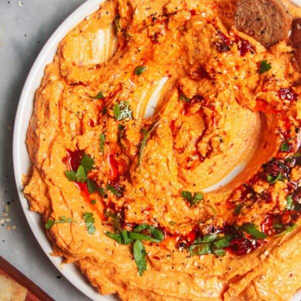 Spicy harissa feta dip on a small white plate, with bagel chips and more harissa on the side.