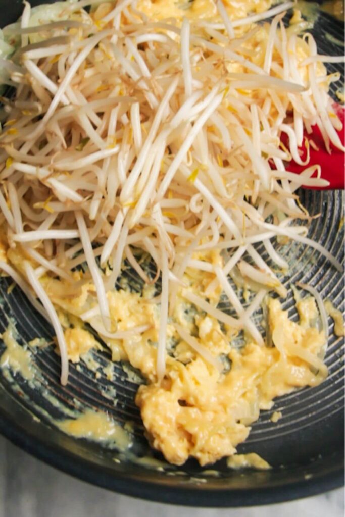 Scrambled eggs and bean sprouts in a large frying pan.