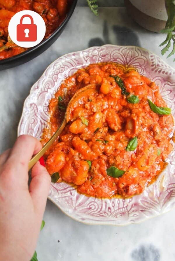 Creamy tomato sausage gnocchi served in a decorative bowl with basil garnish.