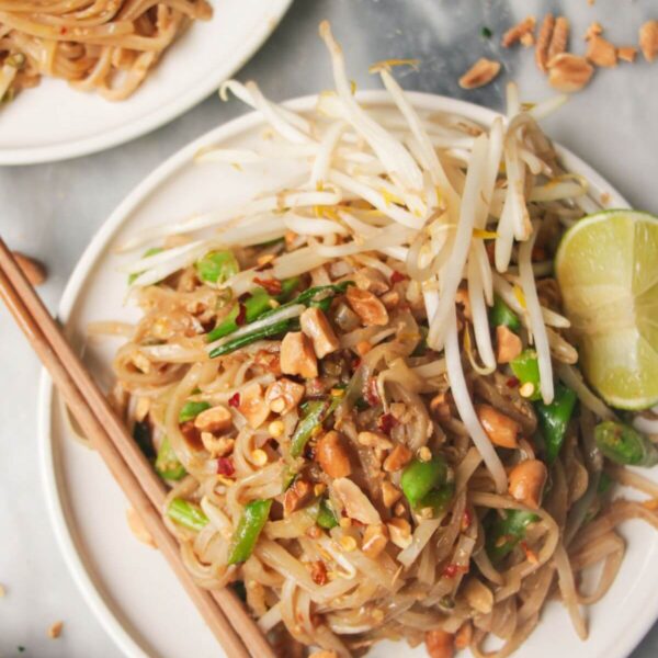 Two plates of pad thai on small white plates, with chopsticks on the side.