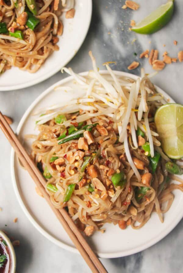 Two plates of pad thai on small white plates, with chopsticks on the side.