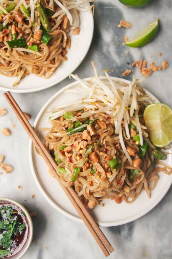 Two plates of pad thai on small white plates, with chopsticks on the side.