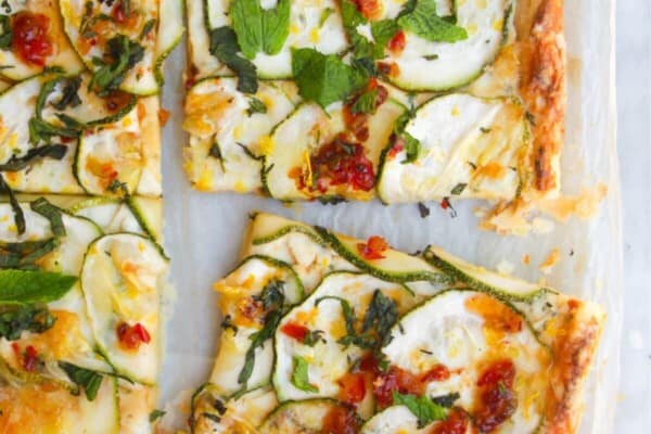 Zucchini puff pastry tart sliced, with a hand pulling one piece out.