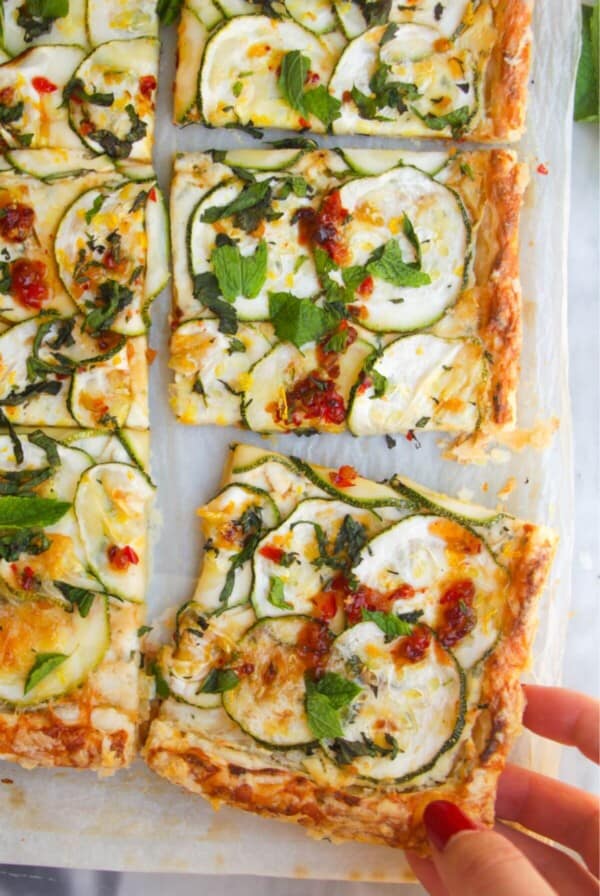 Zucchini puff pastry tart sliced, with a hand pulling one piece out.