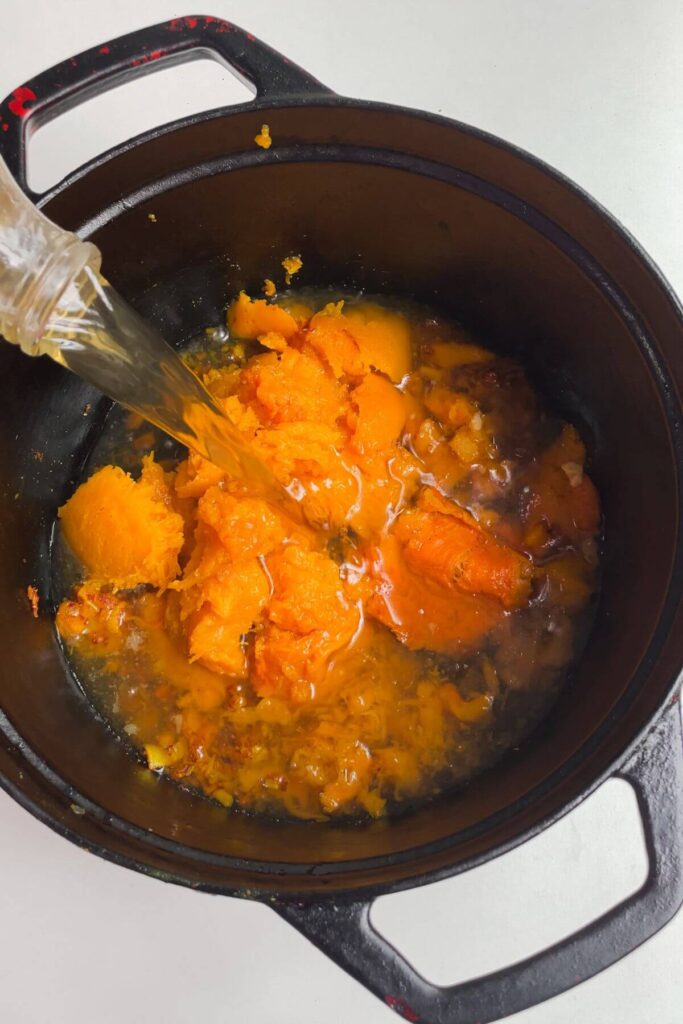 Stock being poured into a large pot with roasted butternut squash in it.