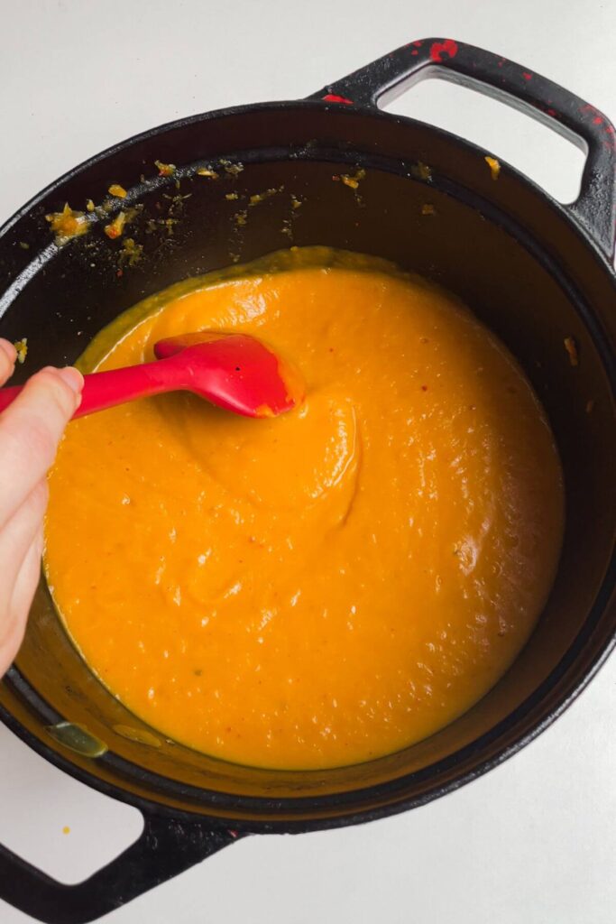 Hand holding a spatula and stirring roasted butternut squash soup.