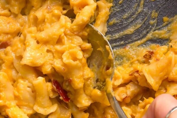 Close up of hand scooping up butternut squash mac and cheese with a large spoon from the pan.