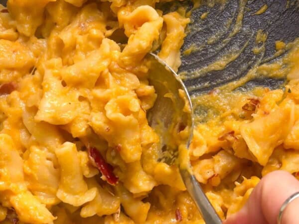 Close up of hand scooping up butternut squash mac and cheese with a large spoon from the pan.