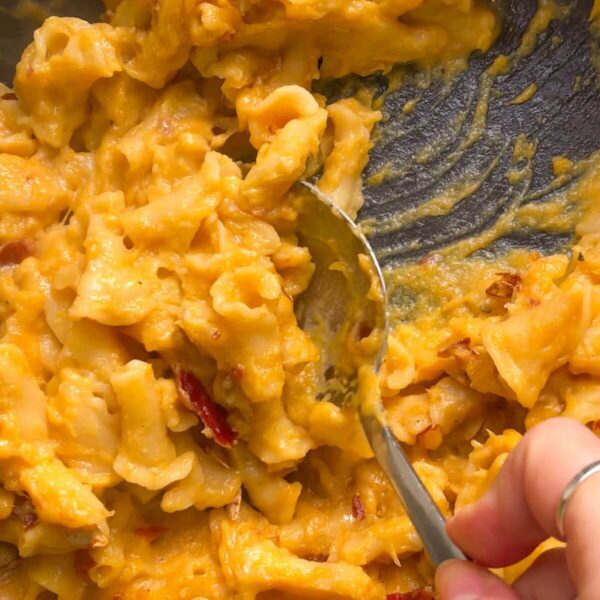 Close up of hand scooping up butternut squash mac and cheese with a large spoon from the pan.