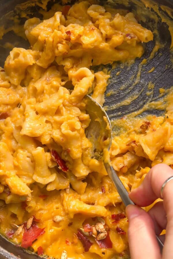 Close up of hand scooping up butternut squash mac and cheese with a large spoon from the pan.