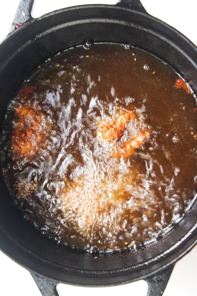 Pieces of chicken frying in a pot of hot oil.
