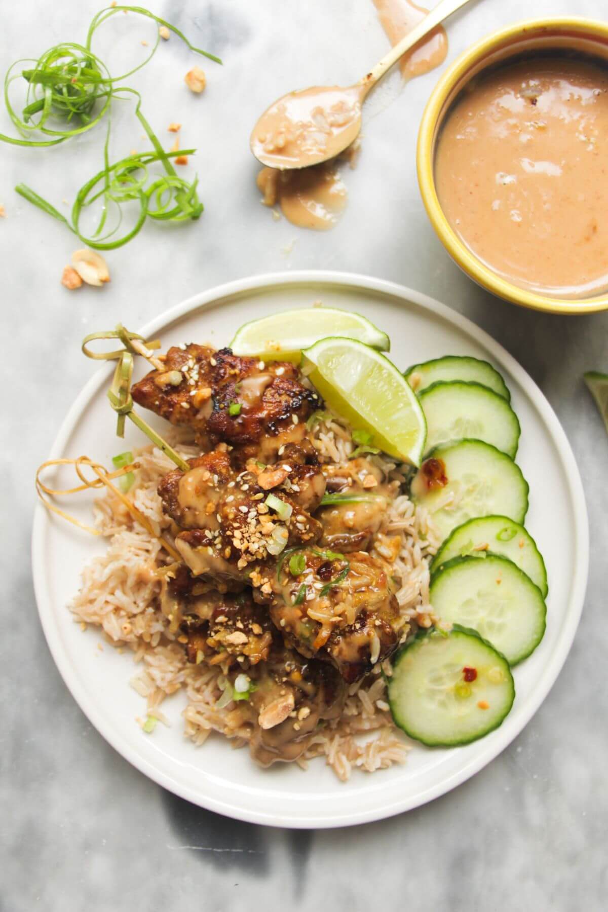 Chicken satay skewers on rice with cucumber slices on the side, with a small bowl of satay peanut sauce behind.