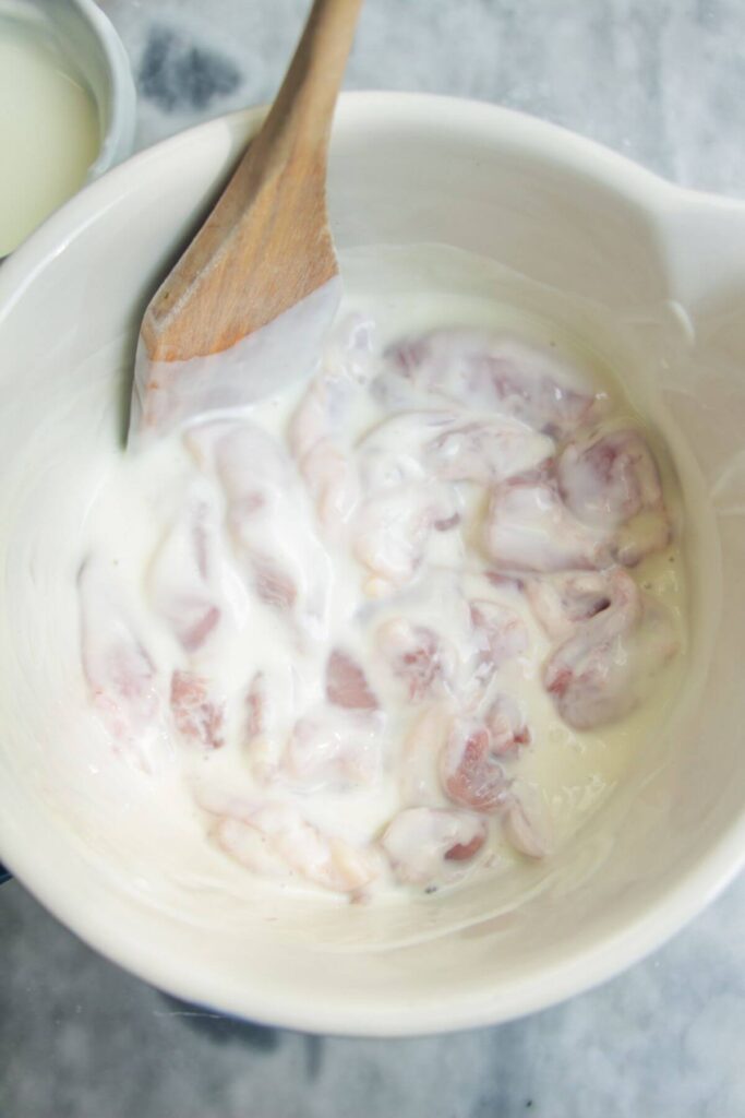 Chicken mixed with yogurt and spices in a large white bowl.