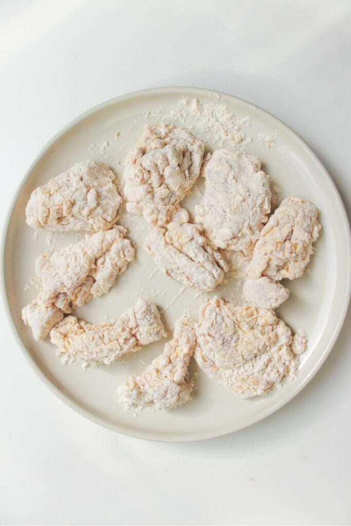Pieces of dredged chicken on a large white plate.