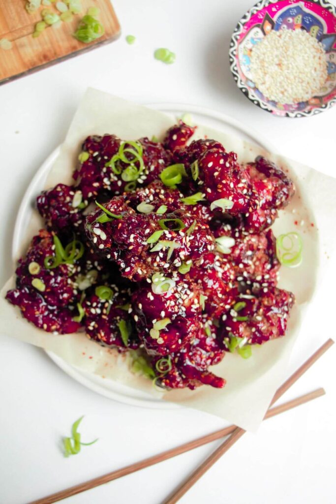 Ple of crispy Korean fried chicken on a small white plate with sesame seeds on the side.