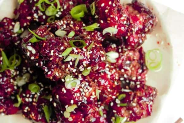 Ple of crispy Korean fried chicken on a small white plate with sesame seeds on the side.