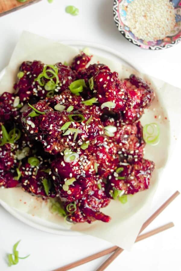 Ple of crispy Korean fried chicken on a small white plate with sesame seeds on the side.