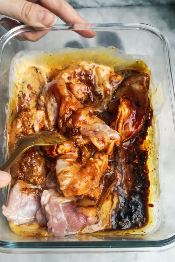 Chicken being mixed through marinade in a glass container.