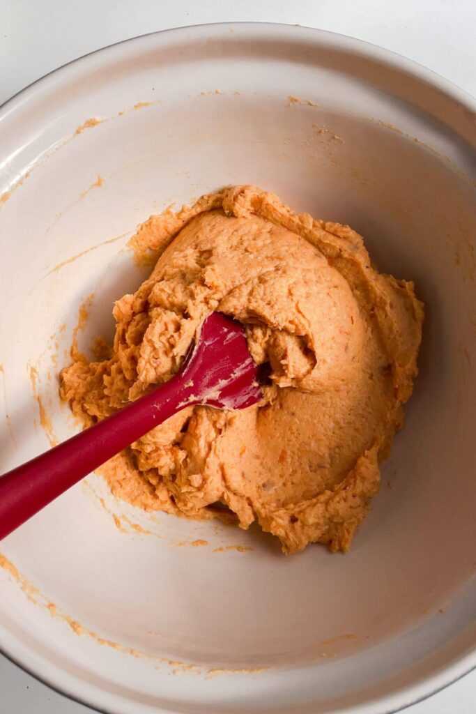 Red spatula stirring sweet potato gnocchi dough in a large mixing bowl.