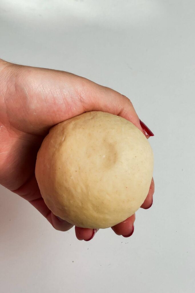 Hand holding kneaded pasta dough ball.