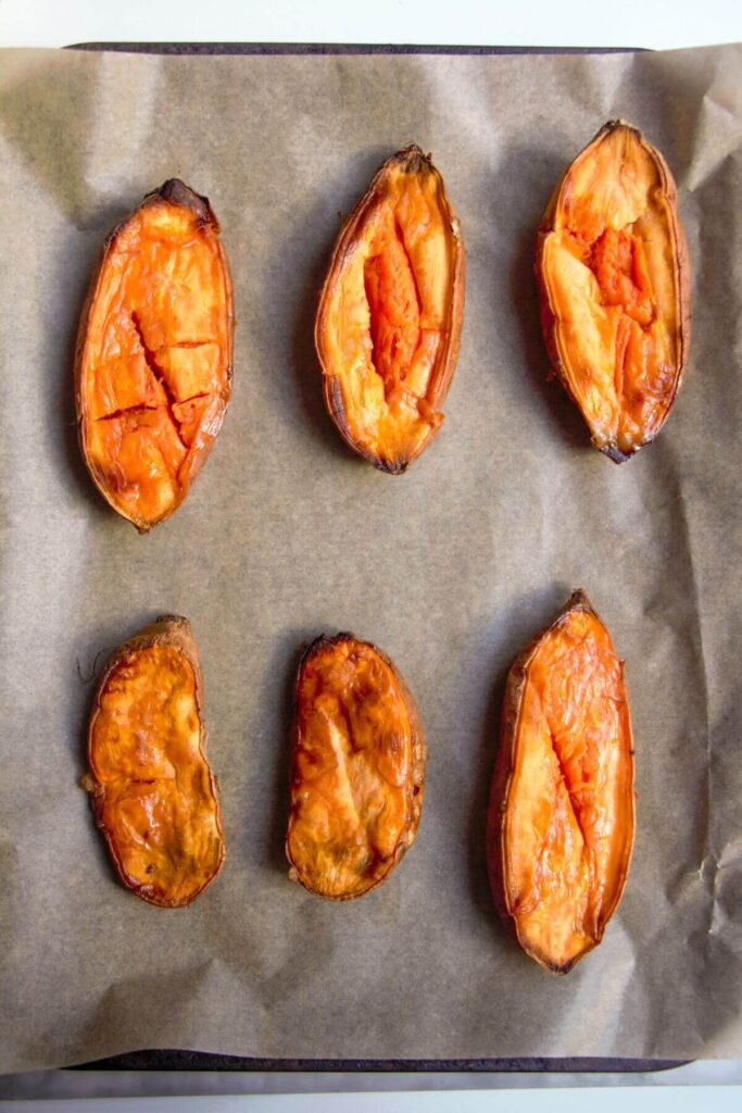 Halved roasted sweet potatoes on a lined tray.