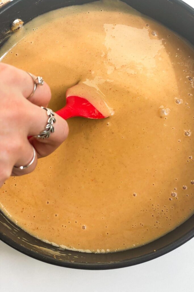 Hand holding spatula stirring peanut satay sacue in a small pan.