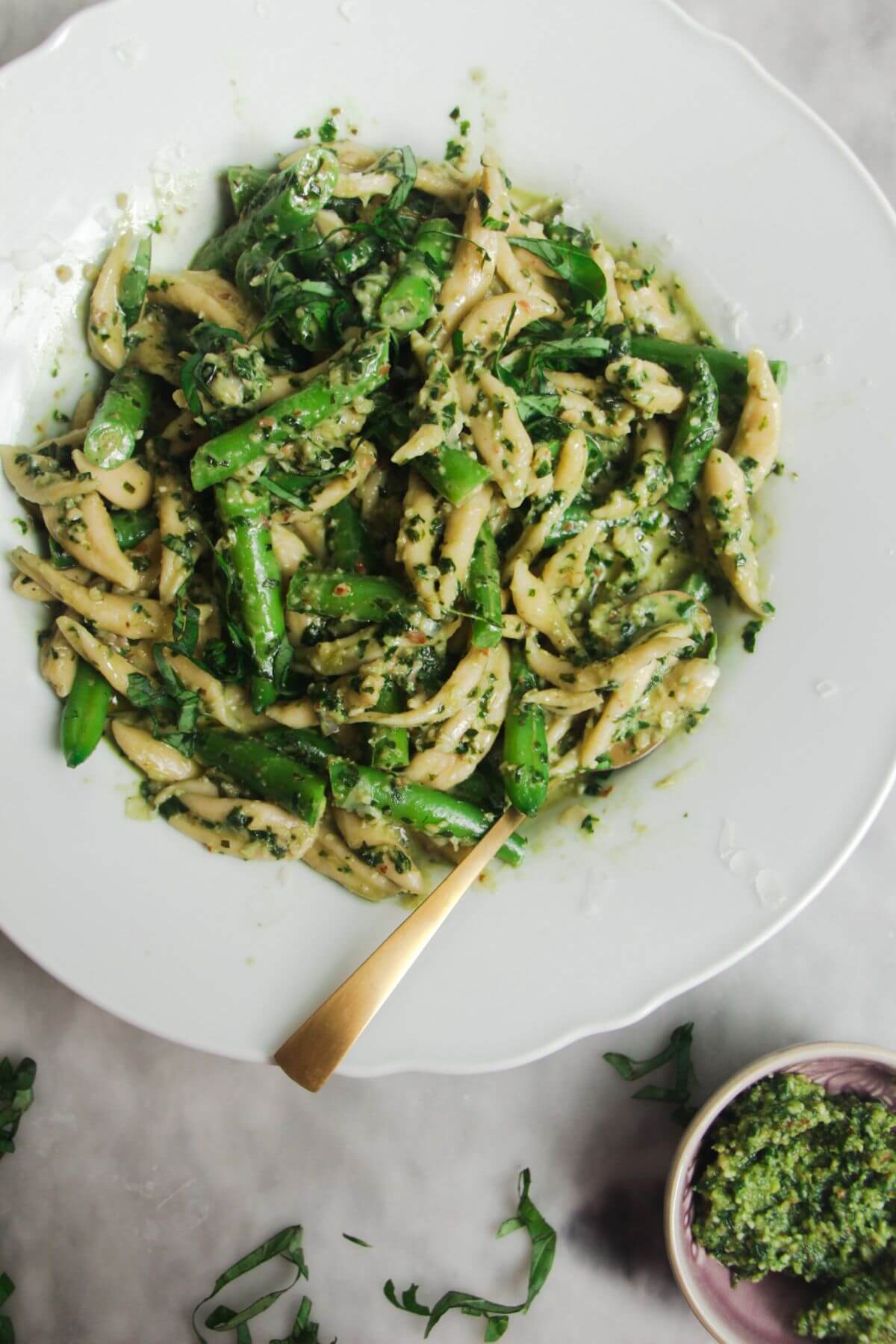 Pesto pasta with green beans in a scalloped plate with more pesto on the side.
