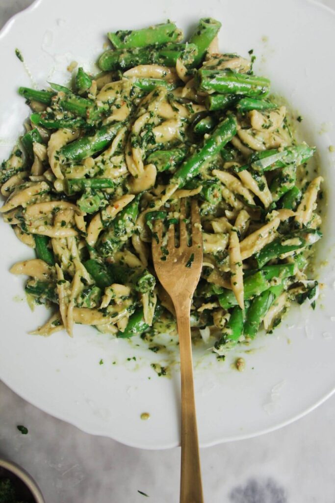 Close up of scissor cut pesto pasta in a white plate with a gold fork.