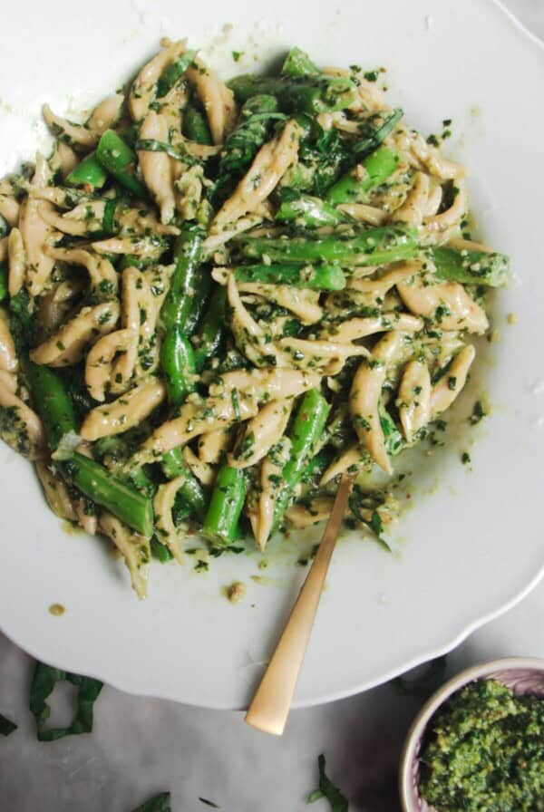 Pesto pasta with green beans in a scalloped plate with more pesto on the side.