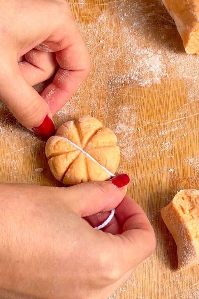 Hands holding string, pressing down on gnocchi dough to create a pumpkin shape.