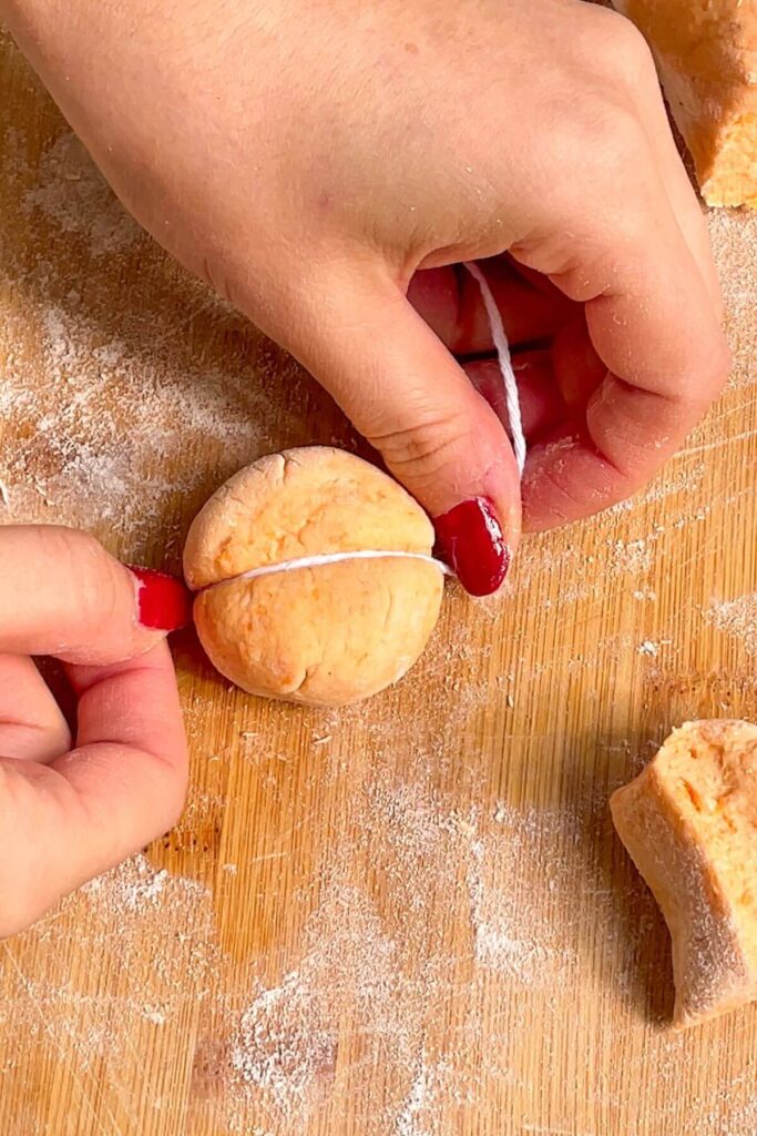 Hands holding string, pressing down on gnocchi dough to create a pumpkin shape.