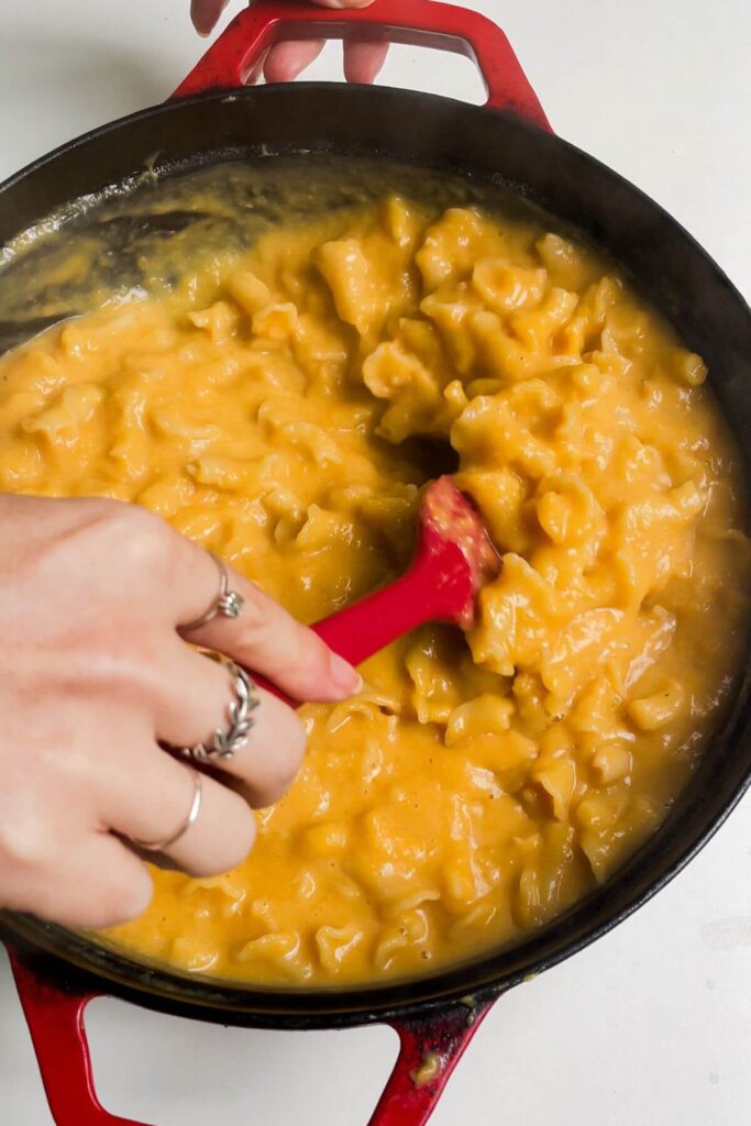 Hand holding a spatula, stirring butternut squash mac and cheese.