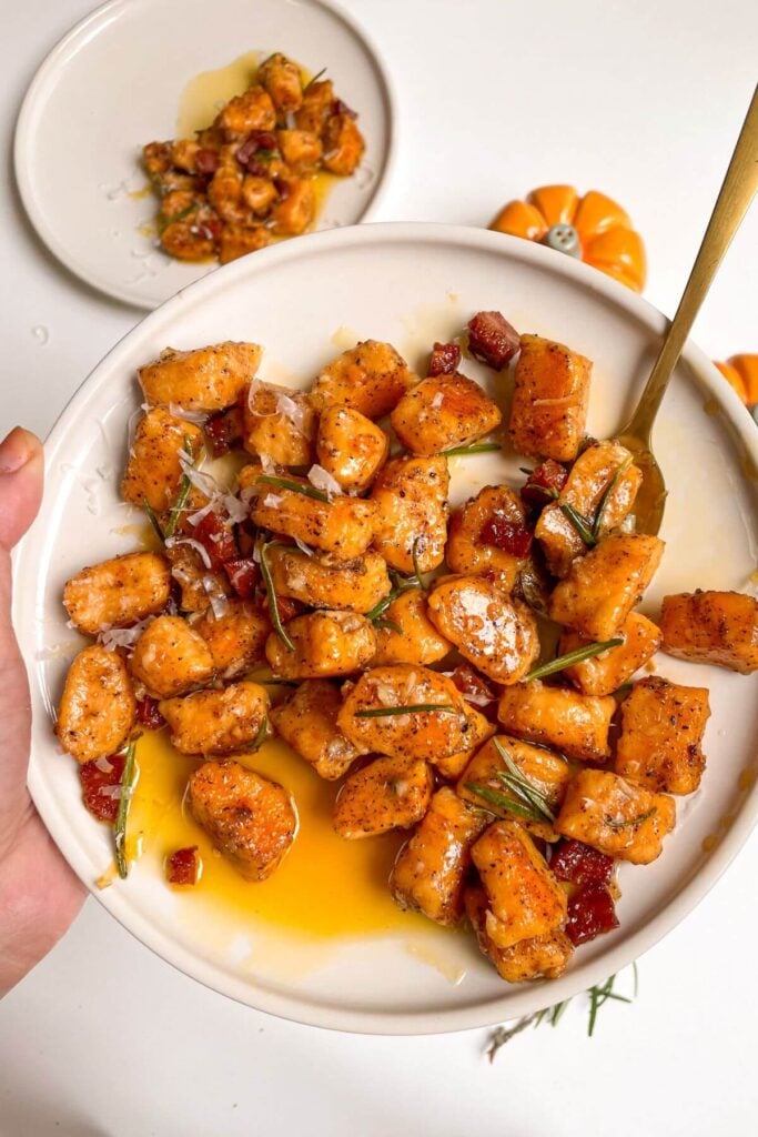 Hand holding a plate of sweet potato gnocchi with a gold spoon in it.