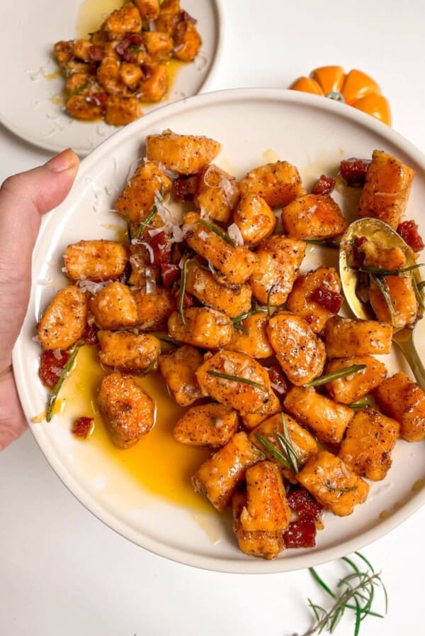 Hand holding a plate of sweet potato gnocchi with a gold spoon in it.