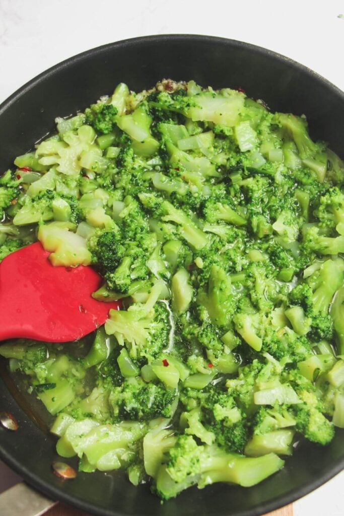 Stirring cooked broccoli in a pan.