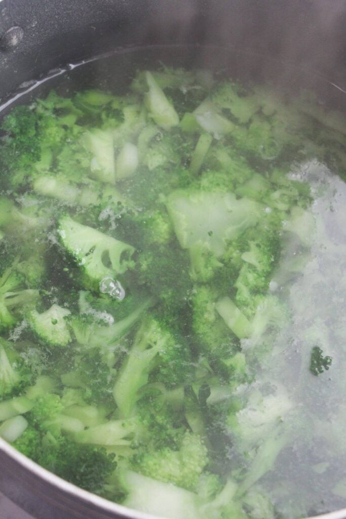 Broccoli florets cooking in a large pot of boiling water.