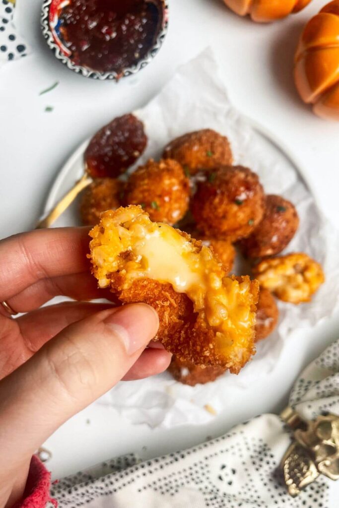 Hand holding torn open arancini, with cheese oozing.