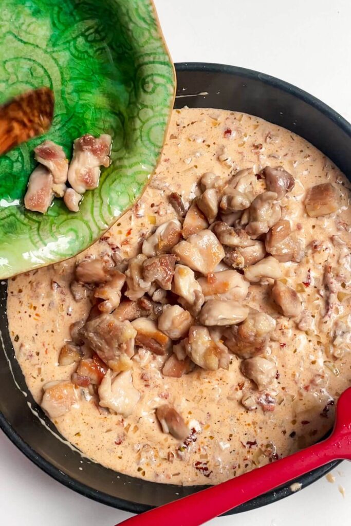 Adding cooked chicken to creamy sauce in a small pan.