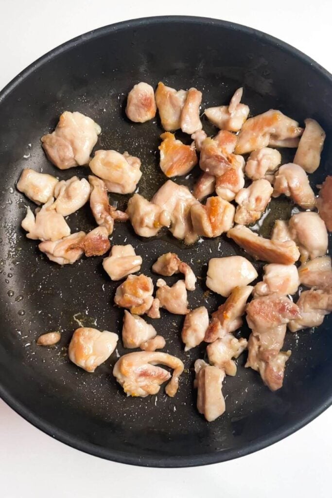 Diced chicken thighs cooking in a small pan.