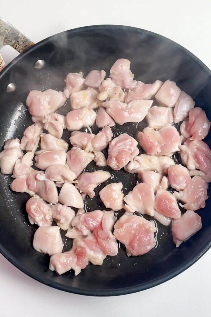 Diced chicken thighs cooking in a small pan.
