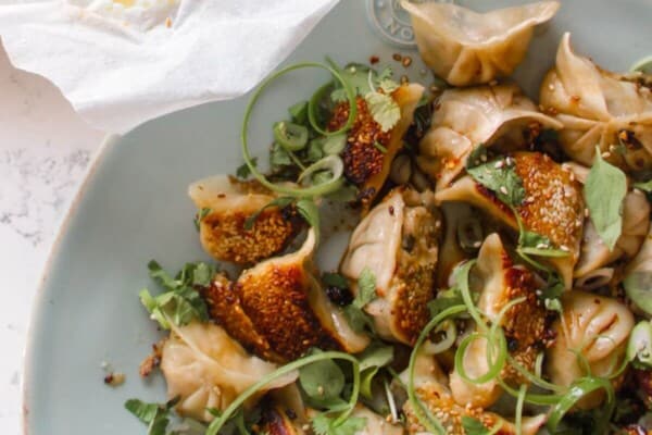 Chicken potstickers on a large blue plate with sauce and steamed buns on the side.